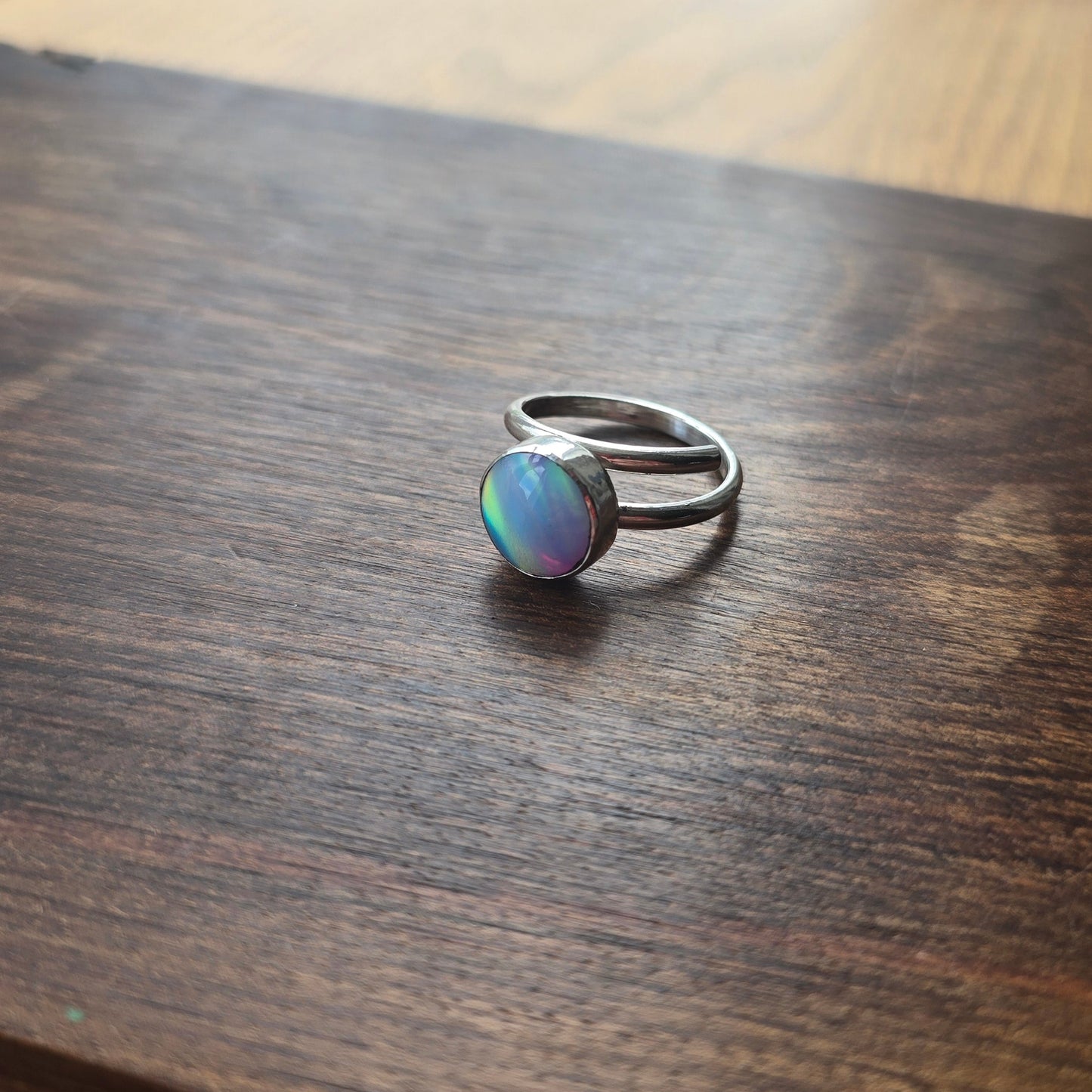 Silver ring with a colorful stone on a wooden surface