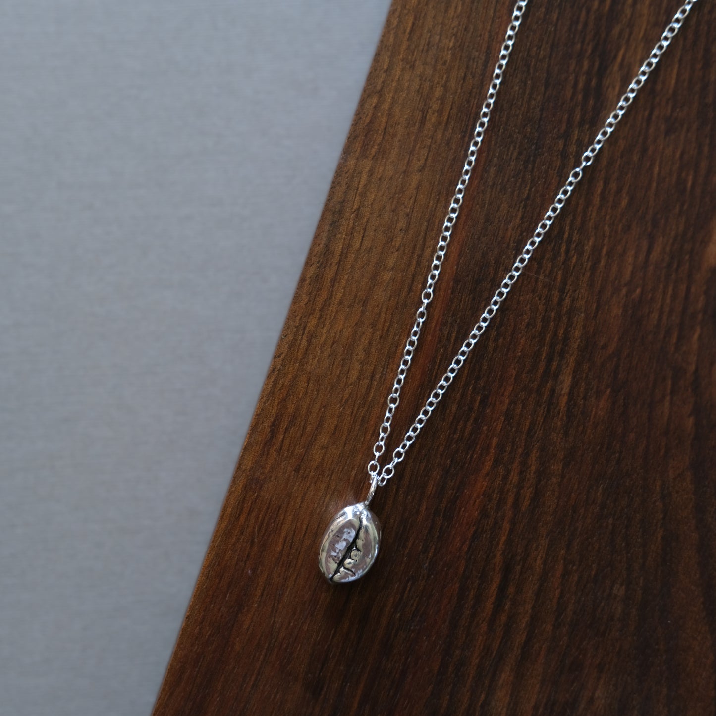 a sterling silver coffee bean necklace sitting on a wooden board