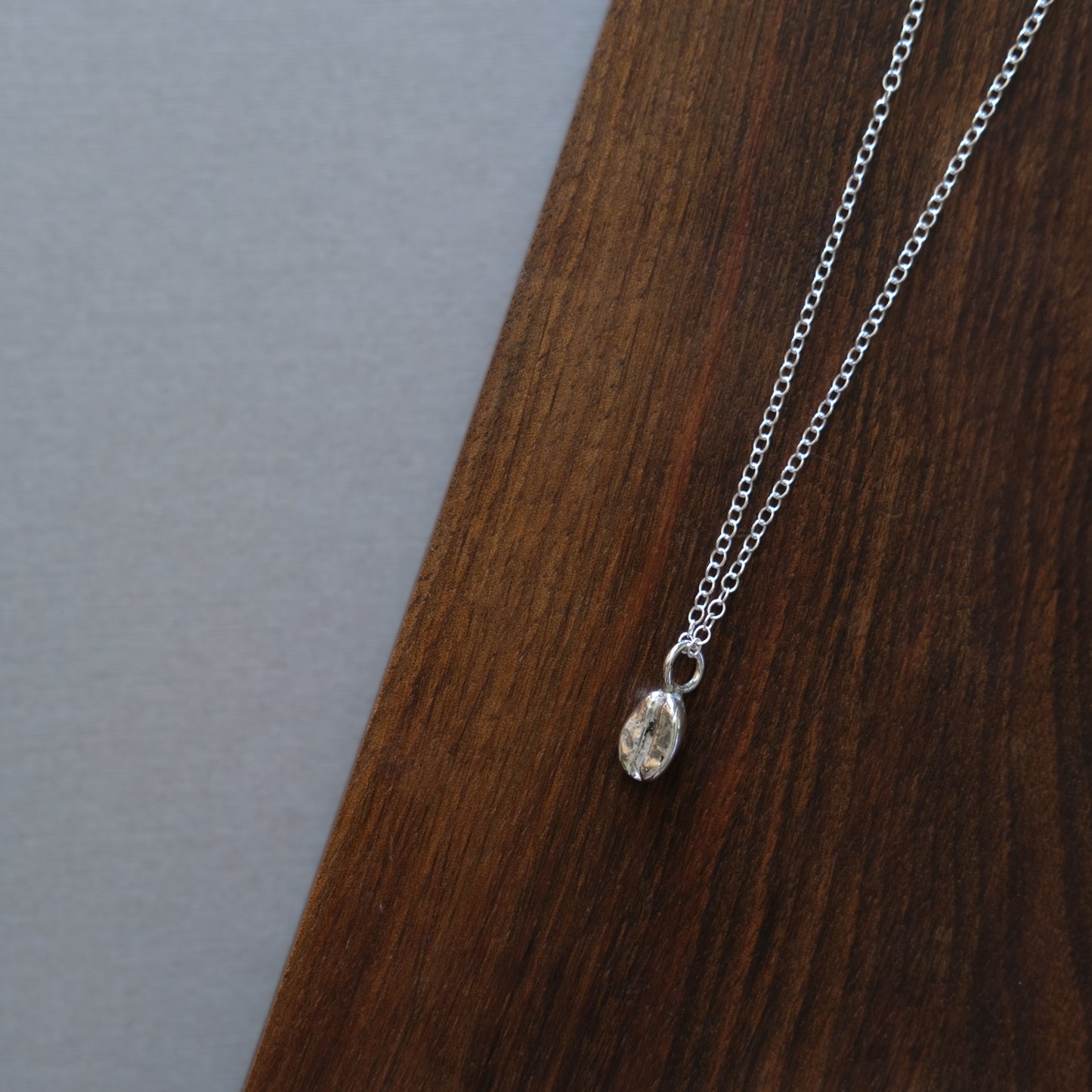 a sterling silver coffee bean necklace sitting on a wooden board