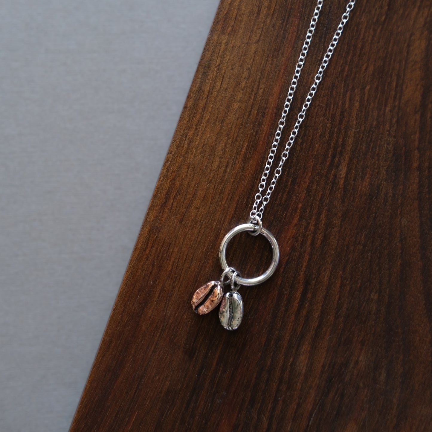a red bronze and sterling silver coffee bean necklace sitting on a wooden board