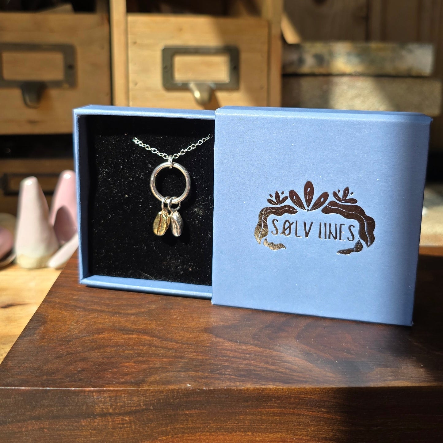 a silver and brass coffee bean necklace boxed up