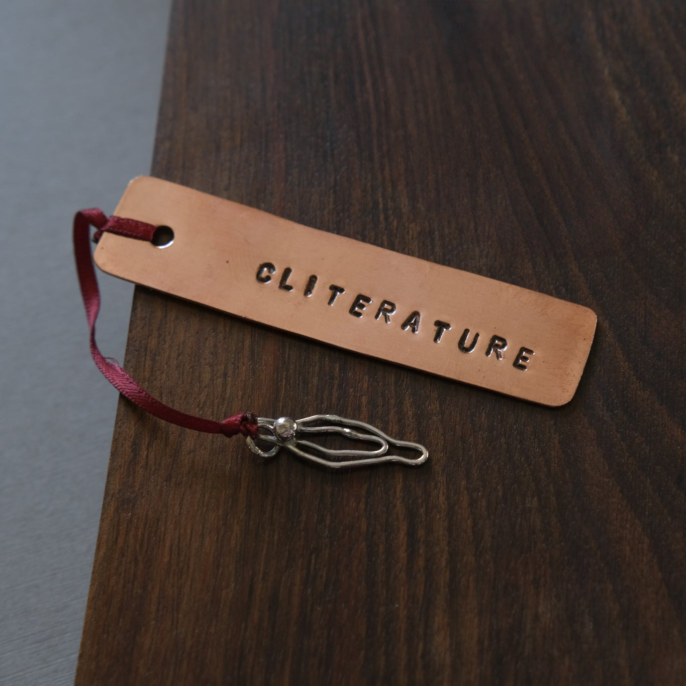 Copper bookmark with 'CLITERATURE' on a wooden surface