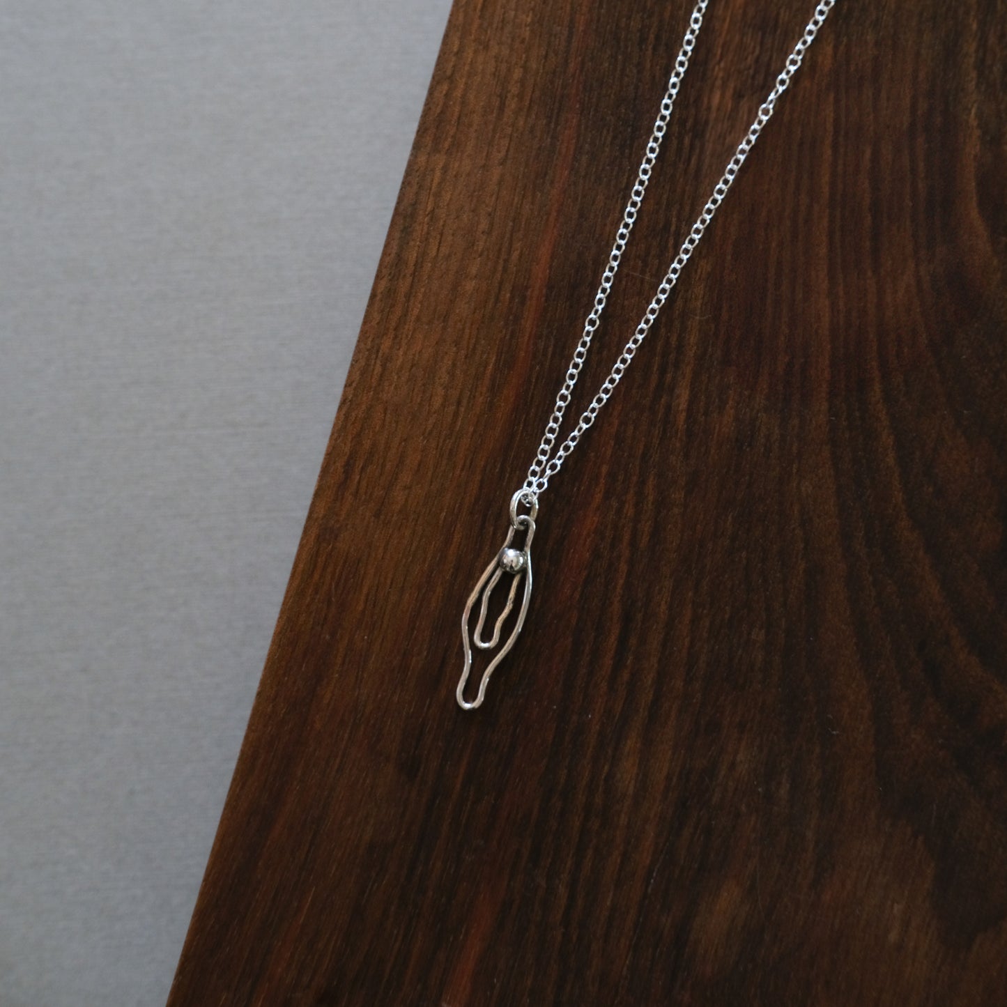 sterling Silver vulva necklace on a wooden surface