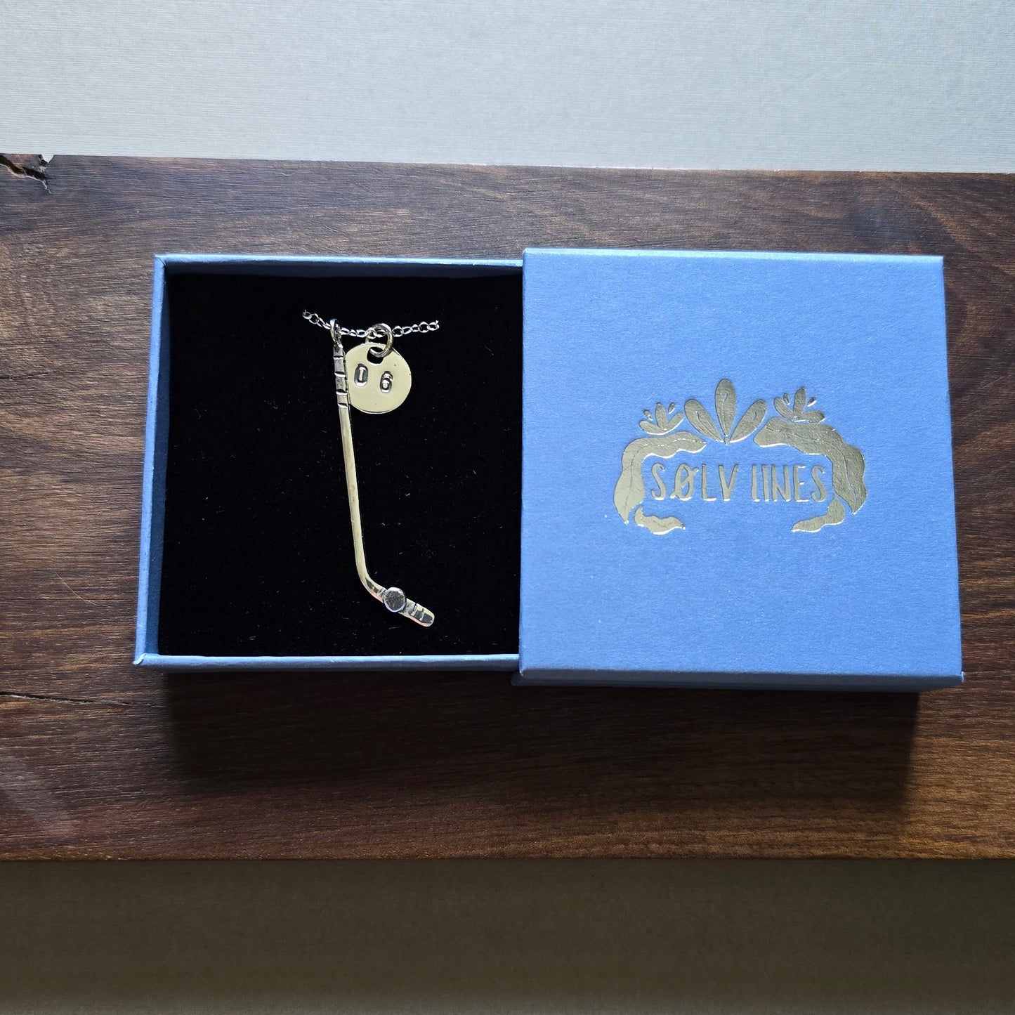 a sterling silver ice hockey necklace with jersey number tag in box