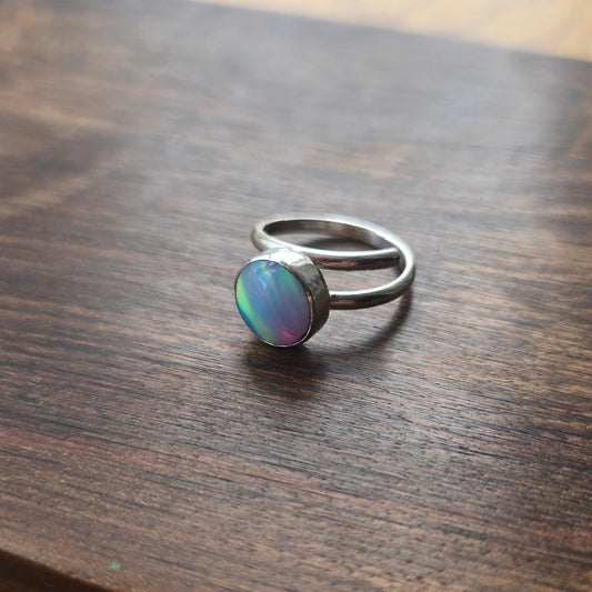 Silver ring with a colorful stone on a wooden surface