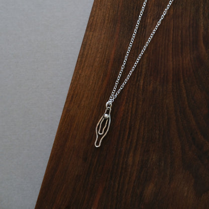 sterling Silver vulva necklace on a wooden surface