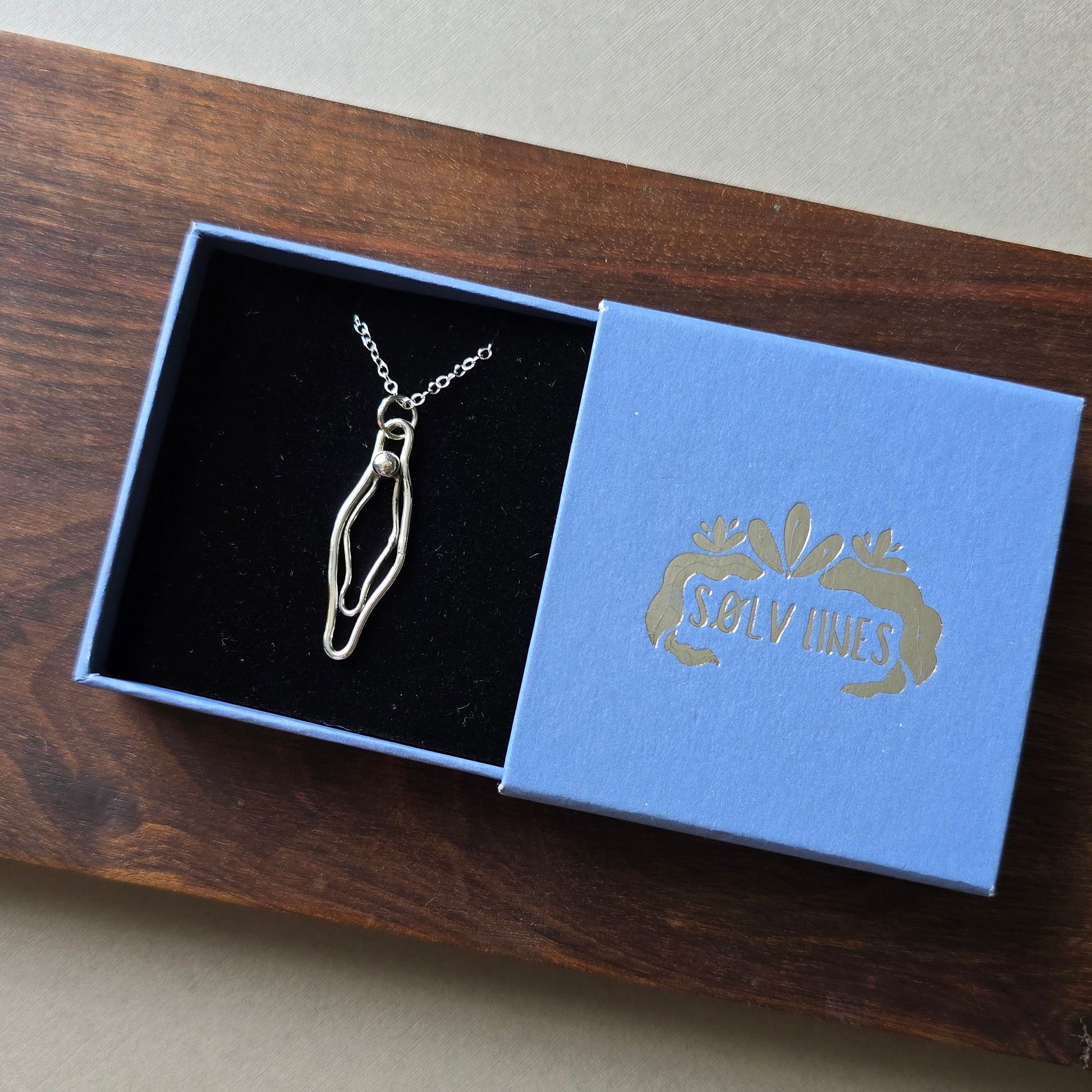 sterling silver vulva necklace in a box on a wooden surface
