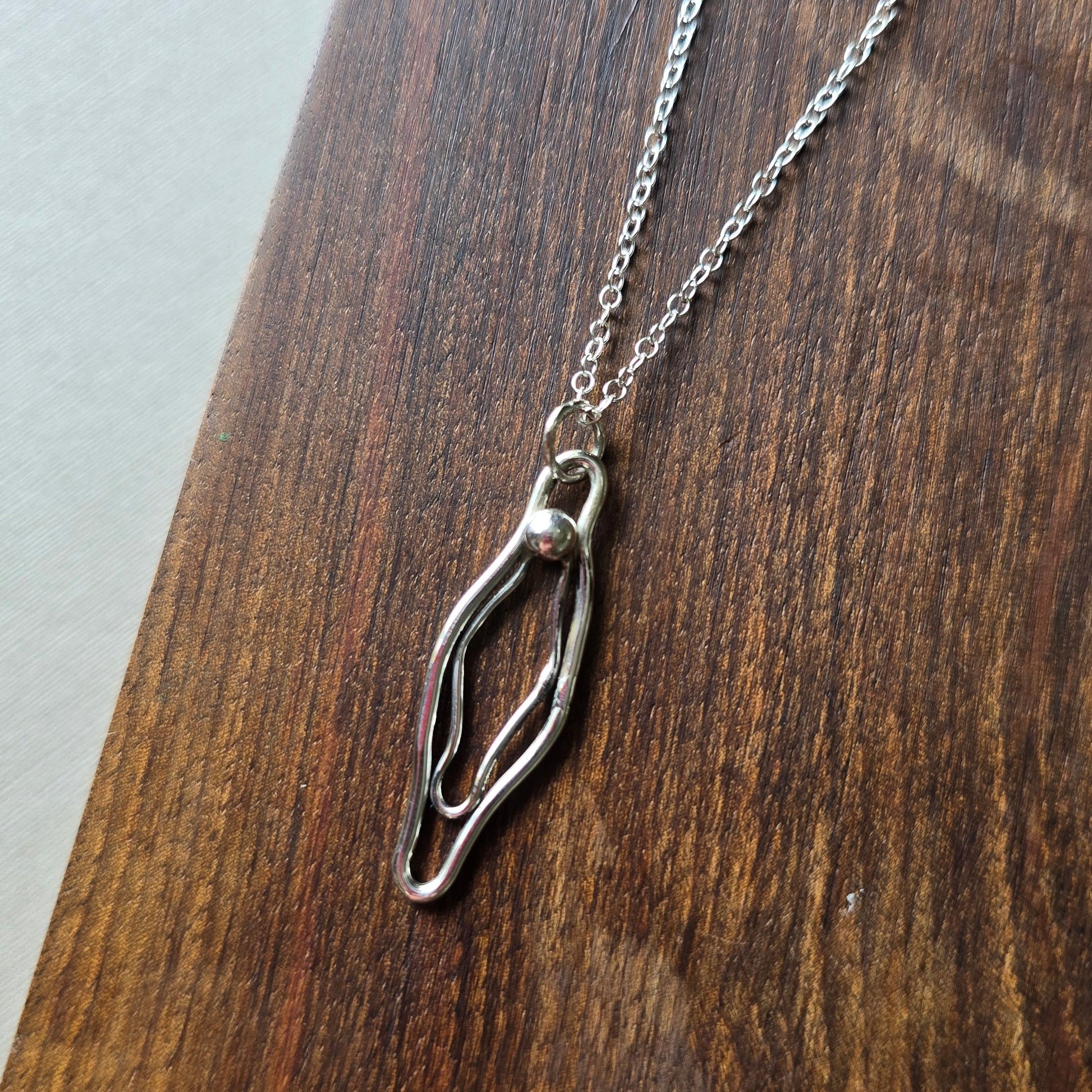 Silver necklace with a vulva pendant on a wooden surface
