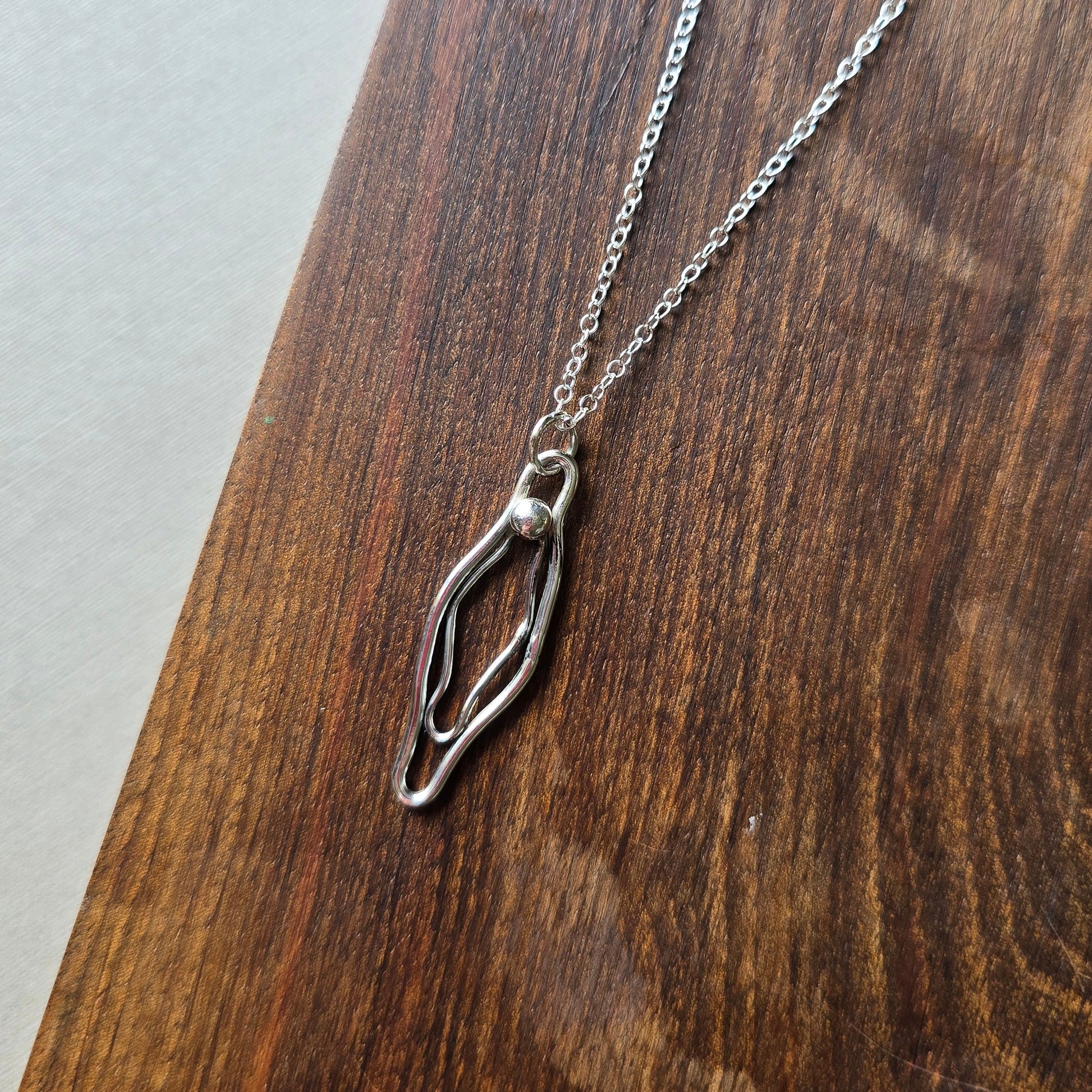 sterling silver vulva necklace on a wooden board