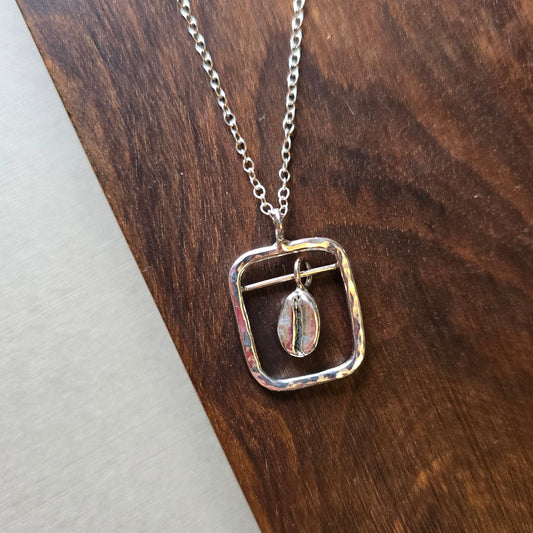 A sterling silver coffee themed necklace with a square silver frame around the bean